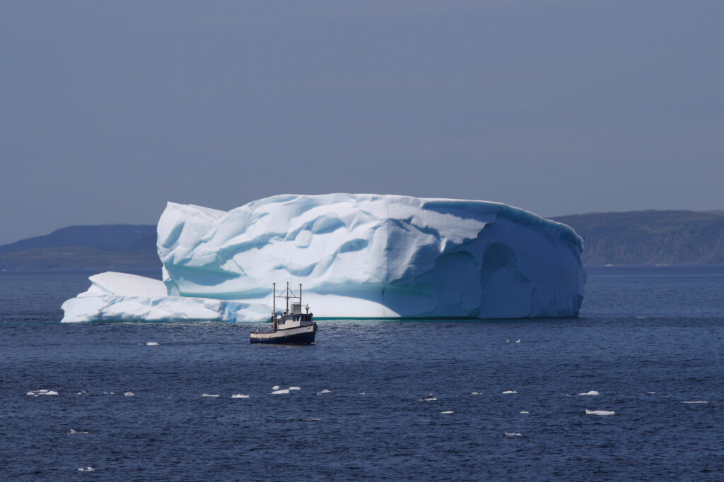 A fishing boat passes an iceberg containing the likeness of a happy face. Goose Cove, Newfoundland, Canada.