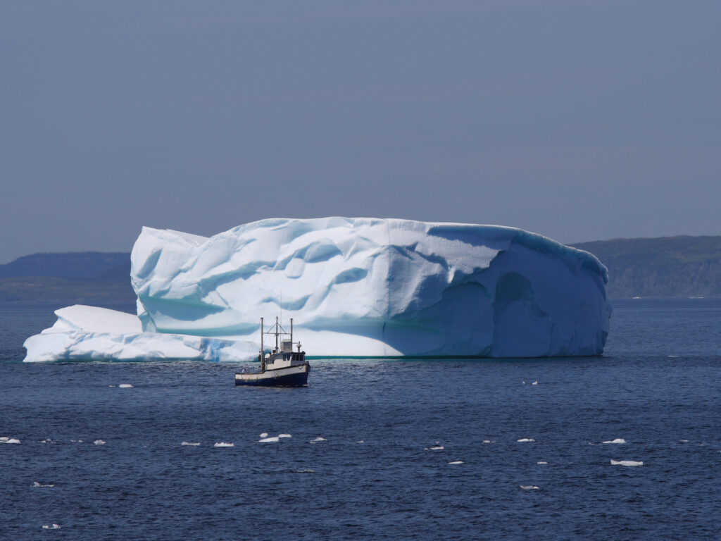 A fishing boat passes an iceberg containing the likeness of a happy face. Goose Cove, Newfoundland, Canada.