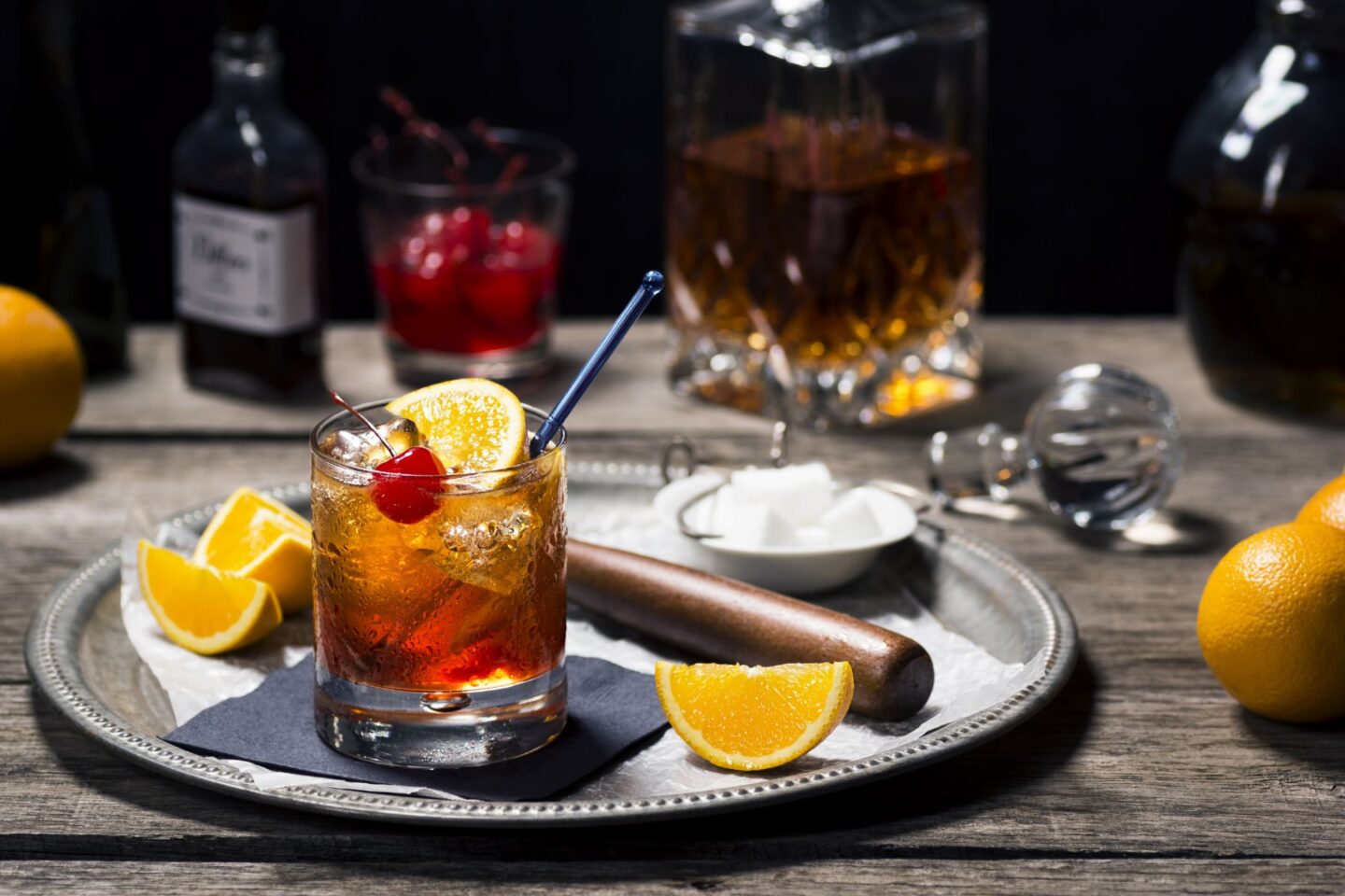 Old Fashioned cocktail garnished with a cherry served on a tray with slices of orange