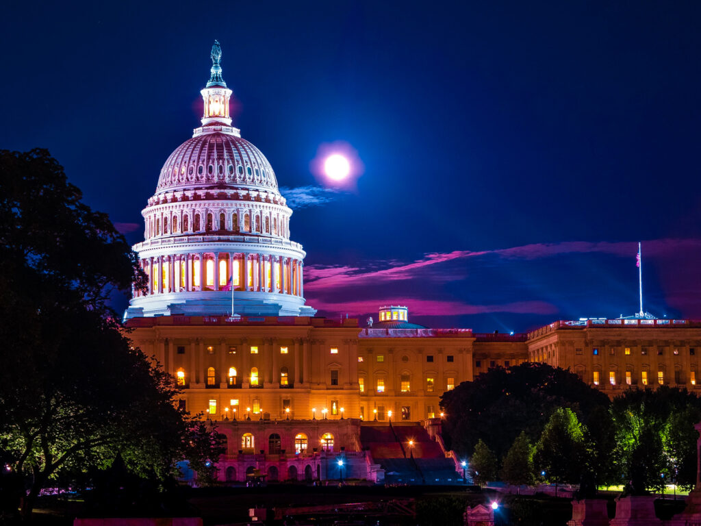 Illuminated dome of the white United States capital building at night with full moon in background