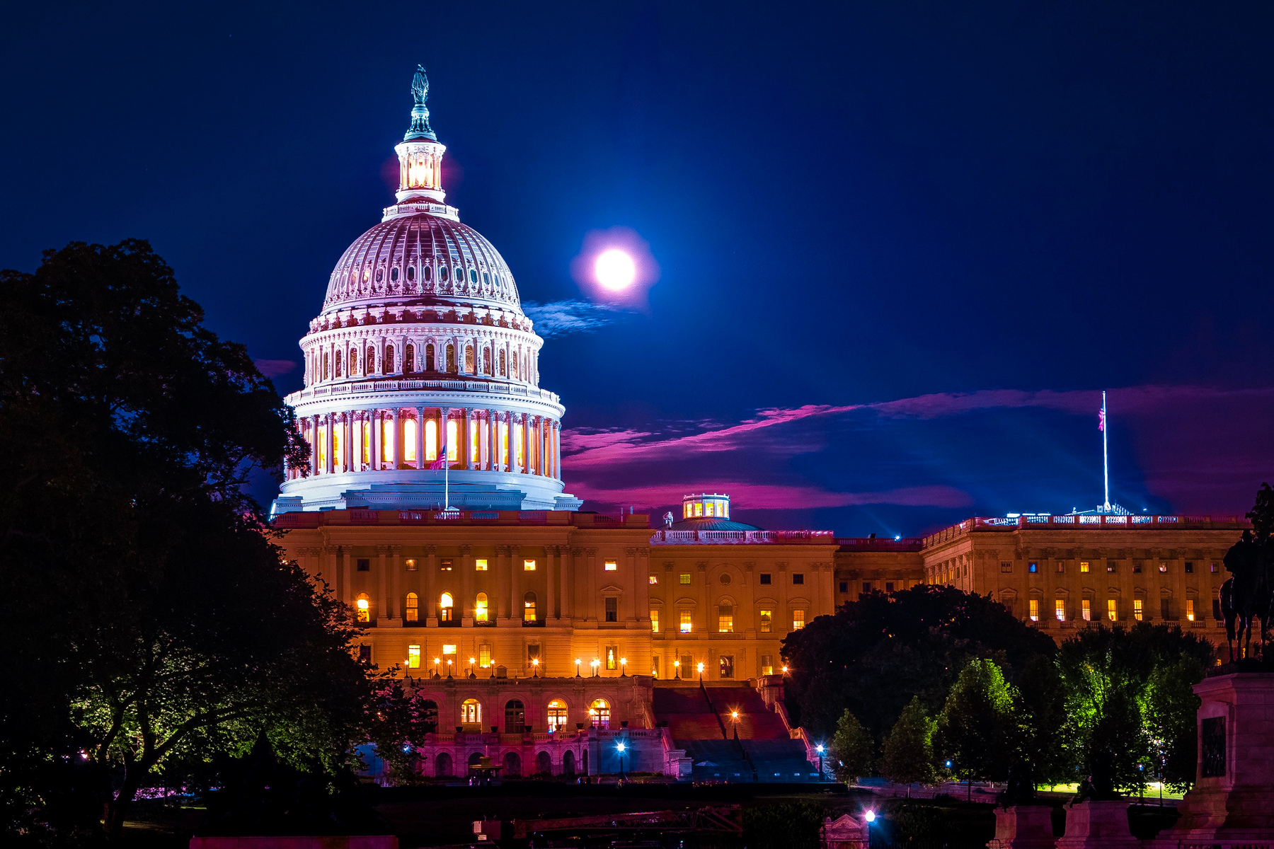 Illuminated dome of the white United States capital building at night with full moon in background